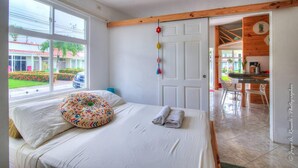 A bedroom with a bed, a window, a door, and a view of the outside. - Romantic Tiny Apartment (Jacó)