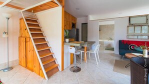 A compact living space with a wooden staircase leading to a loft area, a kitchenette, a dining area with two chairs, and a sofa. - Romantic Tiny Apartment (Jacó)