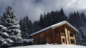 Een houten hut met een schuin dak, omgeven door met sneeuw bedekte bomen.