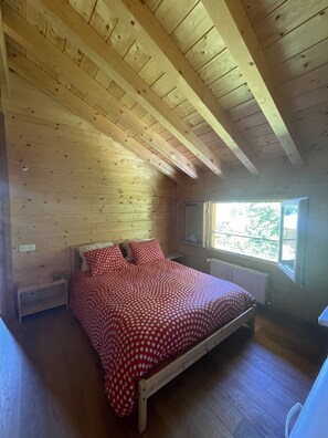 A wooden cabin bedroom with a bed, a window, and a radiator.