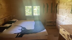 Een houten kamer met een bed, een bureau en twee ramen voor natuurlijk licht.