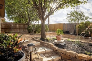 A backyard with a tree, potted plants, and stone steps.