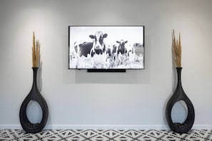 A framed black and white photograph of cows on a wall, flanked by two black vases with dried plants.