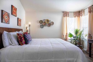 Une chambre à coucher avec un grand lit, des œuvres d’art décoratives accrochées au mur et une plante en pot.