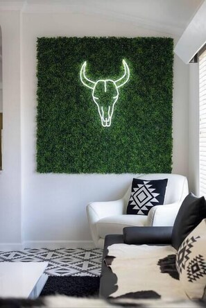 A room with a white sofa, a patterned throw, and a wall-mounted neon bull head decoration. - 🌵 Stylish Hot Tub Oasis 🌵 (San Antonio)