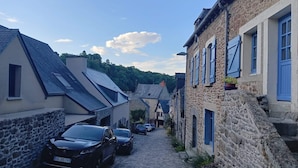 Eine enge Kopfsteinpflasterstraße, gesäumt von Steinhäusern, von denen einige blaue Fensterläden haben, und mit parkenden Autos.