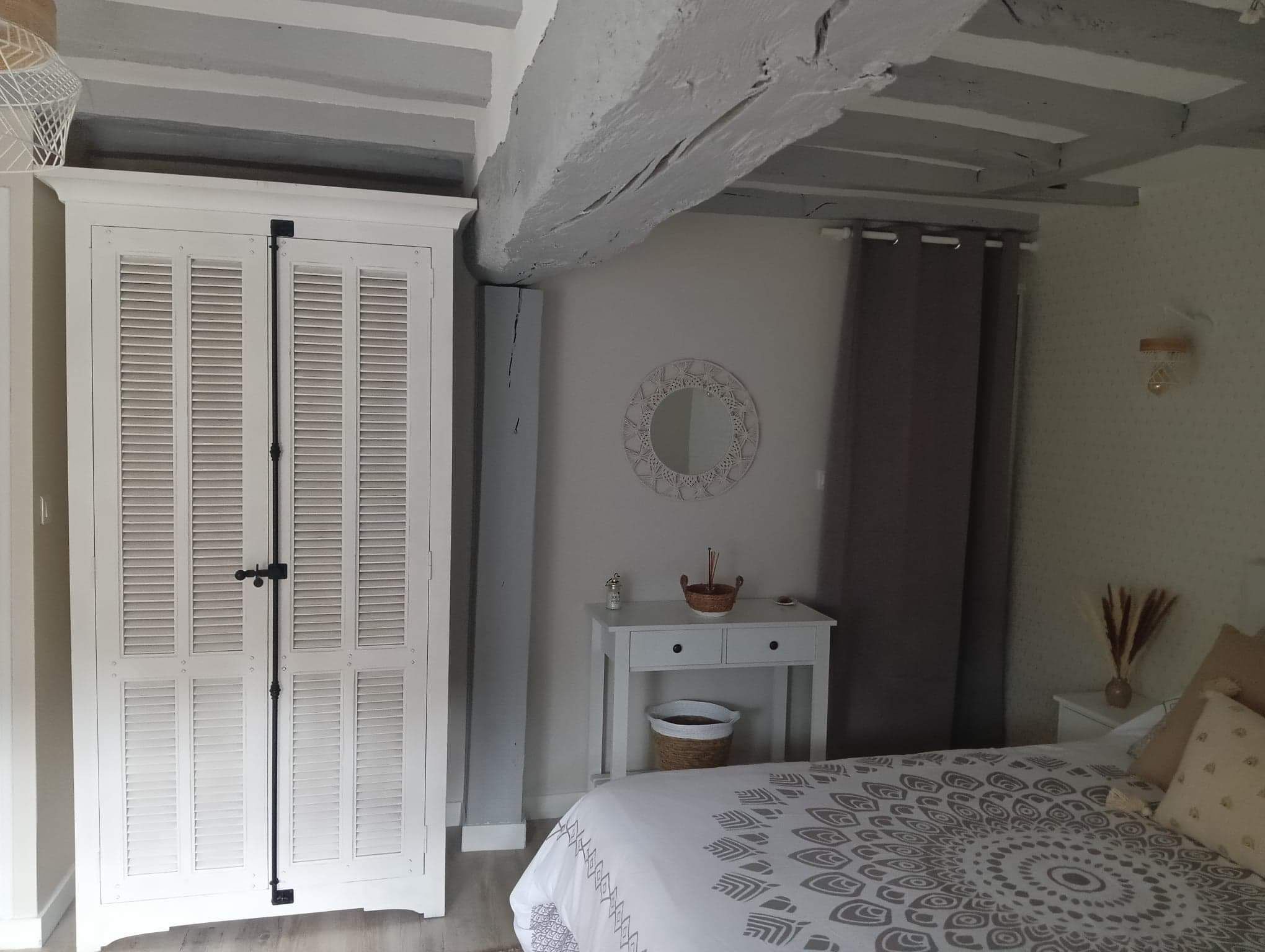A bedroom with a bed, a bedside table, a mirror, and a wardrobe.