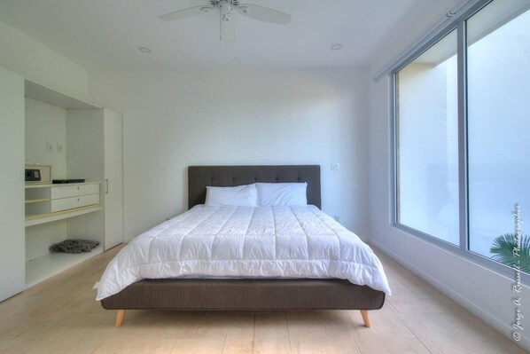 A modern bedroom with a large bed, a wardrobe, and a window with a view. - Beautiful Small Three Bedroom (Jacó)