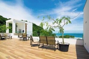 A modern outdoor patio with wooden flooring, metal chairs, and a potted tree. - Beautiful Small Three Bedroom (Jacó)