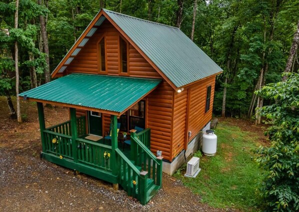 A wooden cabin with a green porch and a metal roof, surrounded by dense forest. - Pets Welcomed at this Colorful Sunflower Cabin. Cooler Mountain Temps Await! (Murphy)