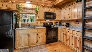 Una cocina con armarios de madera, un refrigerador negro, un microondas y una estufa.