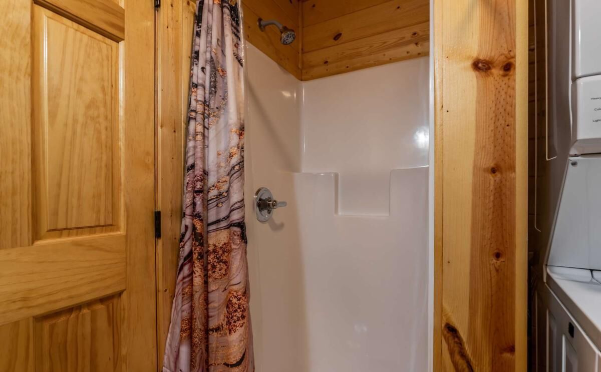 Une porte en bois avec un rideau de douche à motifs, une porte blanche et un plafond en bois.