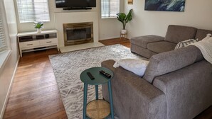 A living room with a grey sofa, a flat-screen TV, a fireplace, and a ceiling fan. - Beach House, 4 Blocks to Ocean/Bay+ BBQ & Firepit! (San Diego)