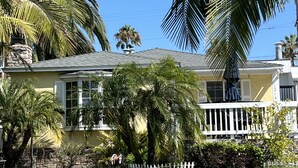 A yellow house with a stone wall in front, surrounded by palm trees and a clear blue sky. - Beach House, 4 Blocks to Ocean/Bay+ BBQ & Firepit! (San Diego)