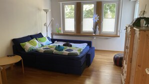 Una habitación con un sofá azul, una mesita, un radiador y una ventana con persianas.