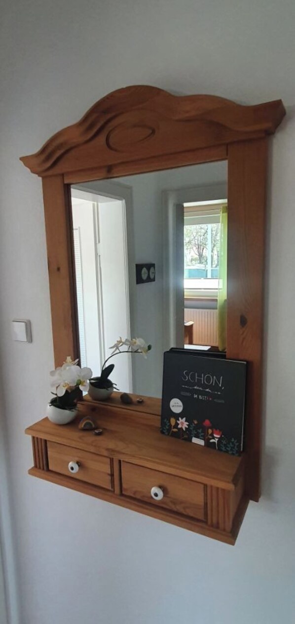 A wooden console with a mirror above it, a small vase with flowers, and a box labeled 'SCHON.'