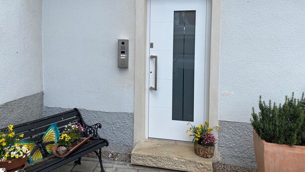 Una puerta blanca con cerradura electrónica, un banco con plantas en macetas y un escalón que lleva a la puerta.