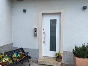 A white door with a keypad lock, a bench with potted plants, and a small step leading to the door.