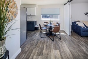 Een moderne keuken met witte kasten, een eethoek met een ronde tafel en stoelen, en een blauwe bank in een woonkamer.