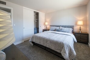 Een slaapkamer met een bed, twee nachtkastjes met lampen, een kledingkast en een vloerbedekking.