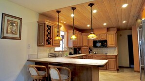 A kitchen with wooden cabinets, a large island with bar stools, pendant lighting, and a microwave. - With tree house, Surprising Tropical-style resort (St. Cloud)