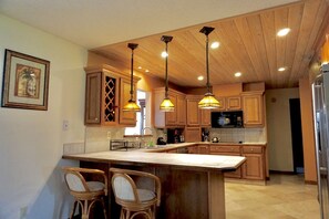 A kitchen with wooden cabinets, a large island with bar stools, pendant lighting, and a microwave. - With tree house, Surprising Tropical-style resort (St. Cloud)