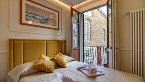 Une chambre d’hôtel avec un grand lit, une tête de lit, un tableau au mur et une vue sur un immeuble par une porte ouverte.