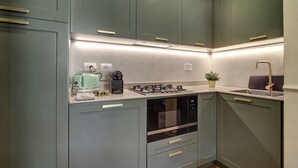 Une cuisine moderne avec des meubles gris, un four encastré, une cuisinière à gaz, une bouilloire et un évier avec un robinet.