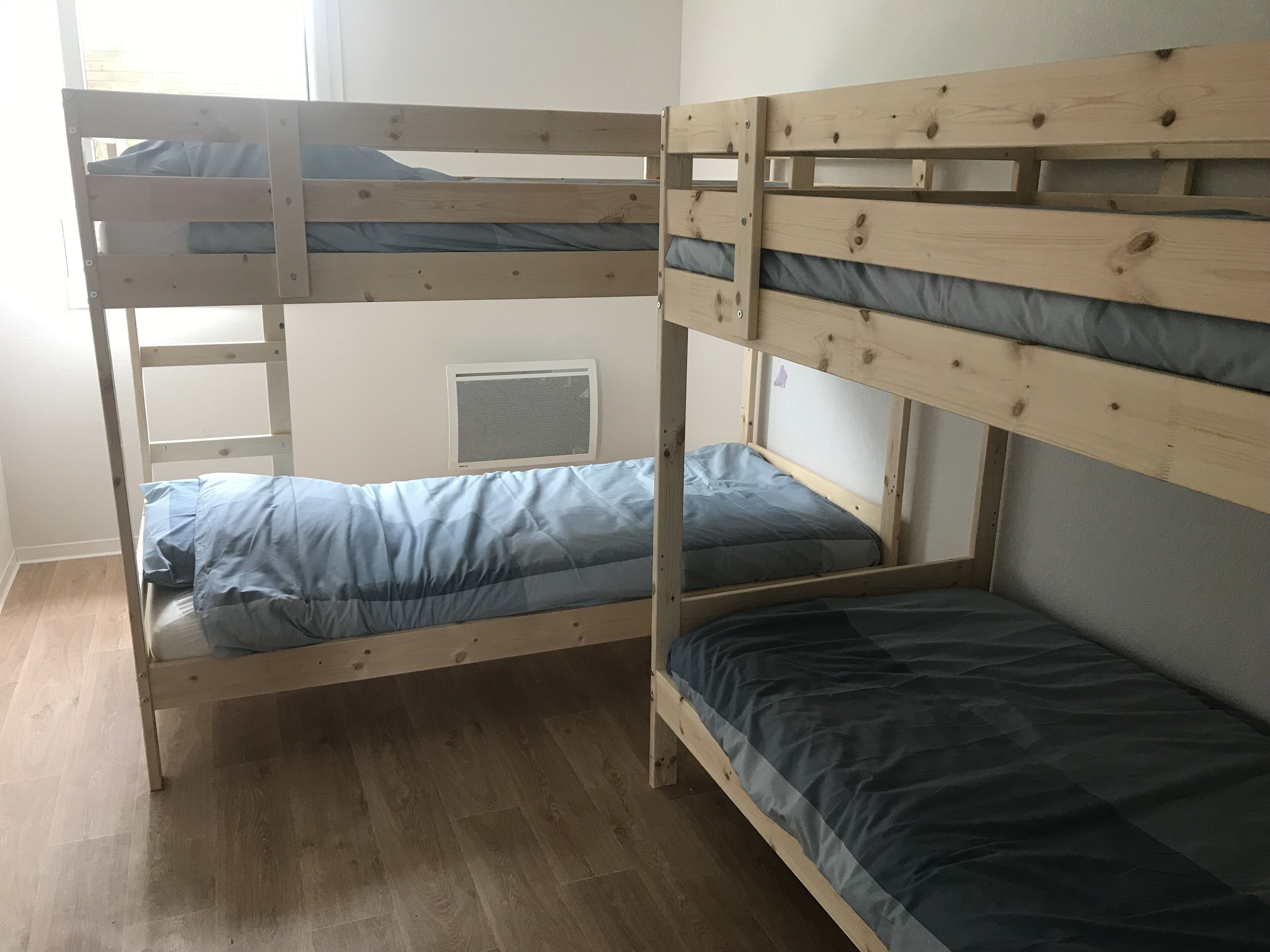 A bunk bed with two levels, a window with blinds, and a radiator on the wall.