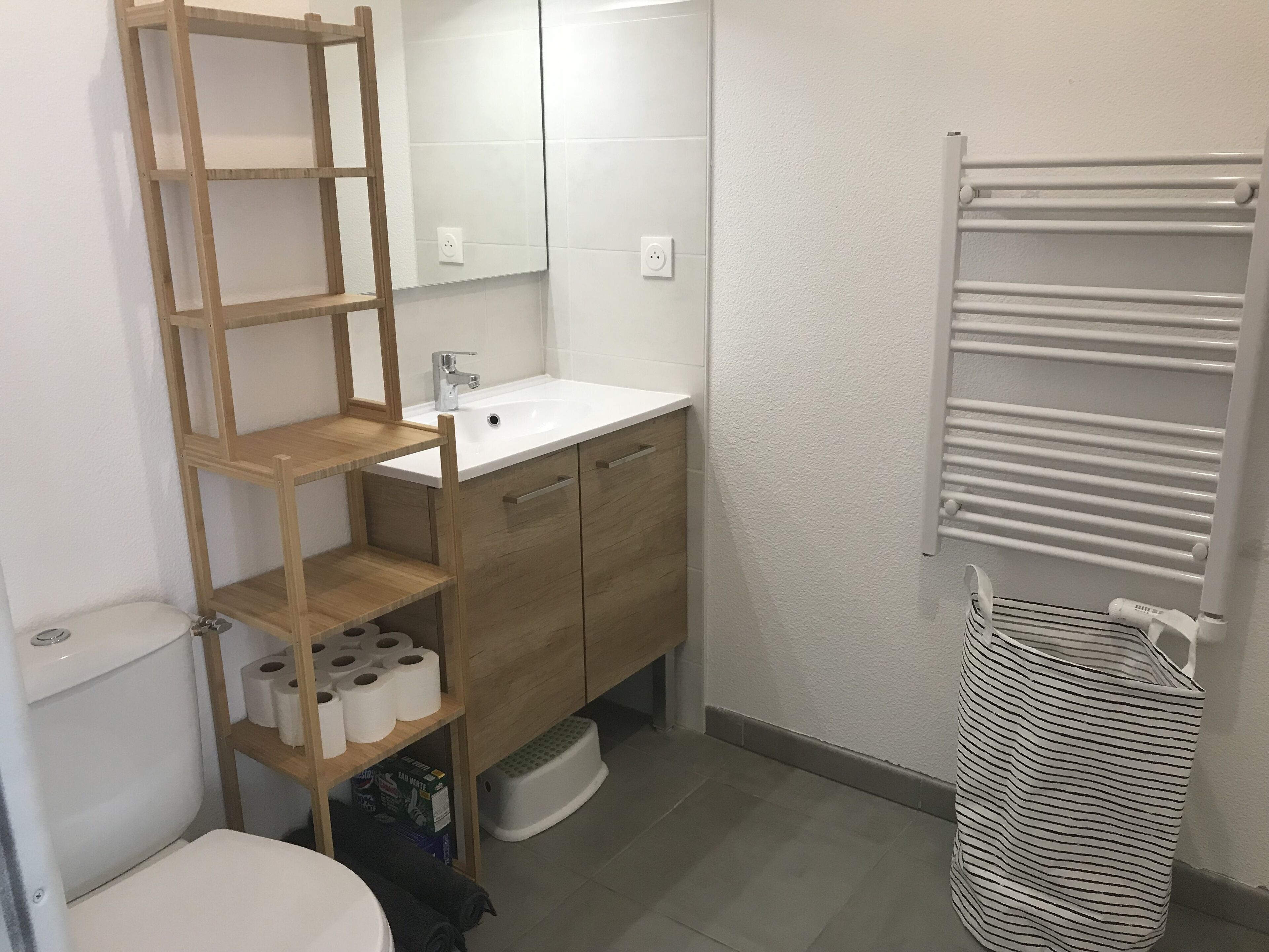 Ein Badezimmer mit einem Holzregal, auf dem Toilettenpapier und ein weißer Handtuchhalter stehen.