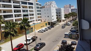 Una calle urbana moderna con edificios de varios pisos, autos estacionados y palmeras.