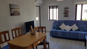 Una sala de estar con una mesa de madera, un sofá azul con cojines, un cuadro en la pared y un cartel con frases motivacionales.