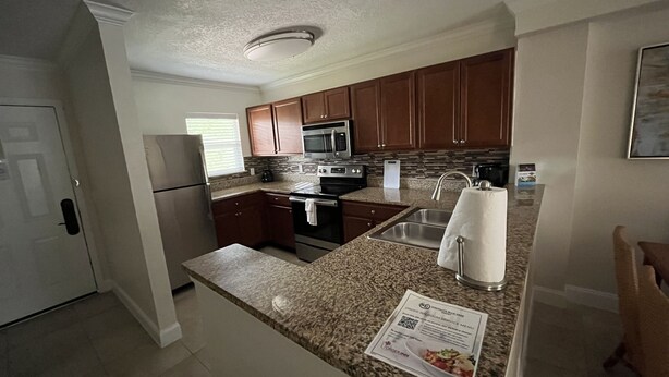 A modern kitchen with granite countertops, stainless steel appliances, and wooden cabinets. - Five minutes from disney world! perfect for family sleeps up to 5-6 with balcony (Orlando)