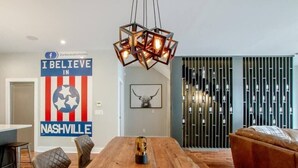 Ein moderner Essbereich mit einem Holztisch, gepolsterten Stühlen und einer hängenden geometrischen Leuchte.