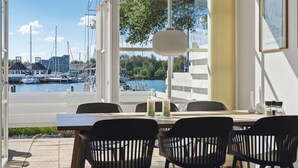 A dining area with a view of a marina, featuring a table with chairs, a hanging light fixture, and a framed picture on the wall. - Stunning home in Ebeltoft with sauna (Ebeltoft)