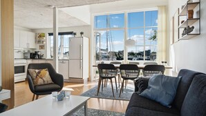 A modern living room with a grey sofa, a dining area with black chairs, and a kitchen with white cabinets and appliances. - Stunning home in Ebeltoft with sauna (Ebeltoft)