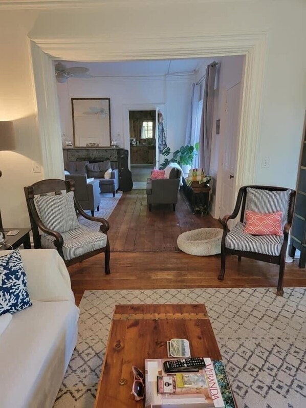 A spacious living room with a wooden floor, two armchairs, a sofa, and a coffee table. A kitchen is visible in the background. - Historic Skye House in the Heart of Northport (Northport)