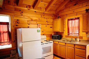 Una cocina tipo cabaña con paredes de madera, un refrigerador blanco, estufa, microondas y gabinetes de madera.