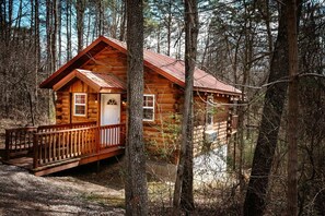 A wooden cabin with a porch and a red roof, surrounded by trees.