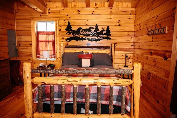 A log cabin bedroom with a bed, a window with curtains, a wall-mounted coat rack, and a decorative wall piece.
