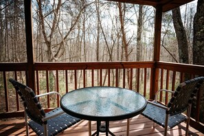A covered outdoor area with a round glass table and two chairs.