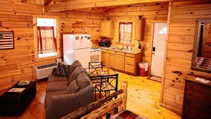 Een kamer in een chalet met een bank, eettafel, keukenhoek en een raam met gordijnen.