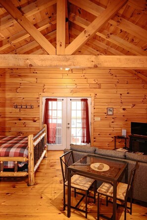L’intérieur d’une cabane en rondins, avec un lit en mezzanine, un canapé, une table à manger en verre et un téléviseur.