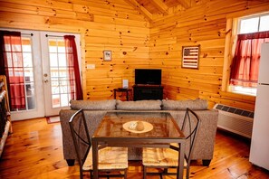 A wooden cabin interior with a sofa, a glass-top table, a television, and a flag on the wall.