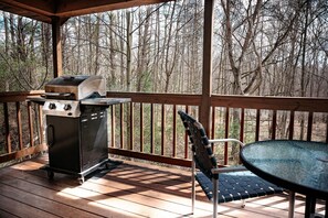 A covered outdoor area with a grill, a table, and a chair.