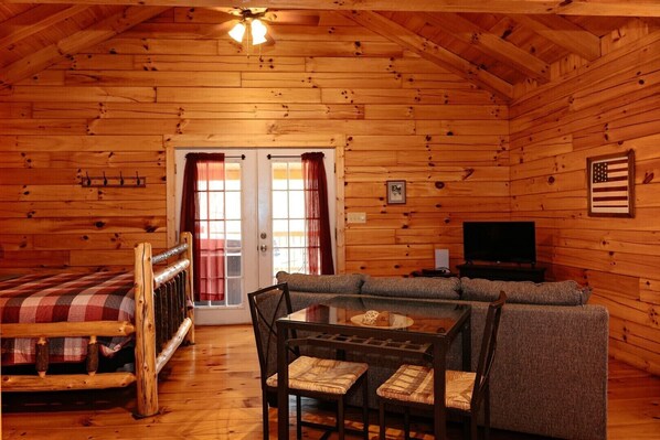 Interior de una cabaña de troncos con sofá, mesa de comedor y televisor.