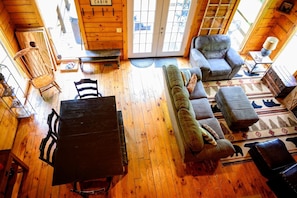 A cabin interior with a wooden dining table, sofa, and ottoman, a bench, and a small table with a lamp.