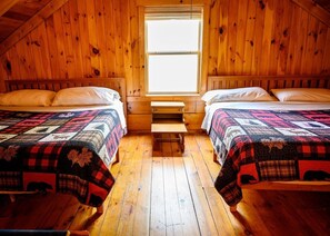A cabin with two beds, a window, and a wooden floor.