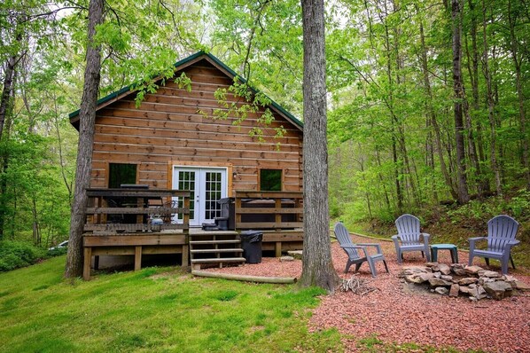 A wooden cabin with a porch, outdoor seating, and a stone fireplace.