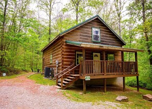 A wooden cabin with a porch, a staircase leading to the entrance, and a gravel path.